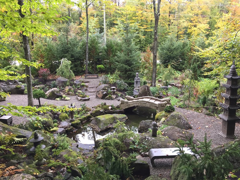 Jardin d'inspiration asiatique, à Lac-Brome : le bassin en eau, le pont de pierre cambré et sa balustrade sculptée, la pagode-lanterne et les pierres moussues, sous la forêt d'automne.