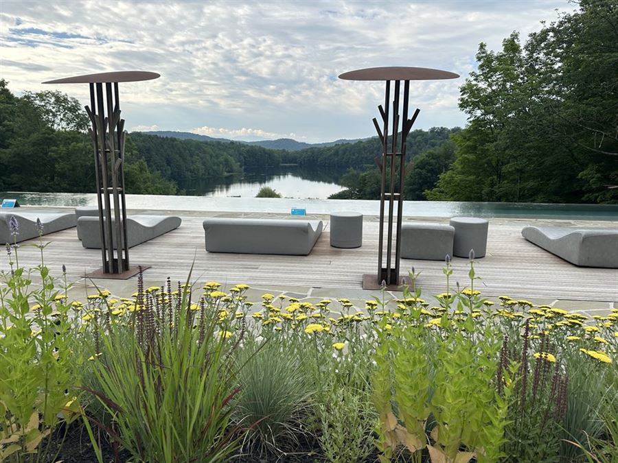 Terrasse de Balnea, à Bromont : bordure de fleurs jaunes et de graminées au premier plan, pontage de bois avec ses chaises longues, puis les bassins, le lac et les montagnes.