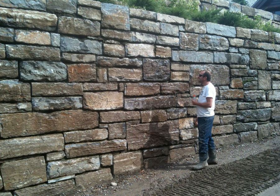 Grand mur de soutènement en pierre naturelle, appareillé bloc par bloc.